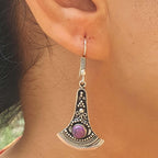 Close-up of a silver earring with a purple gemstone worn by a person.