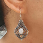 Ornate silver earring with a white stone worn by a person