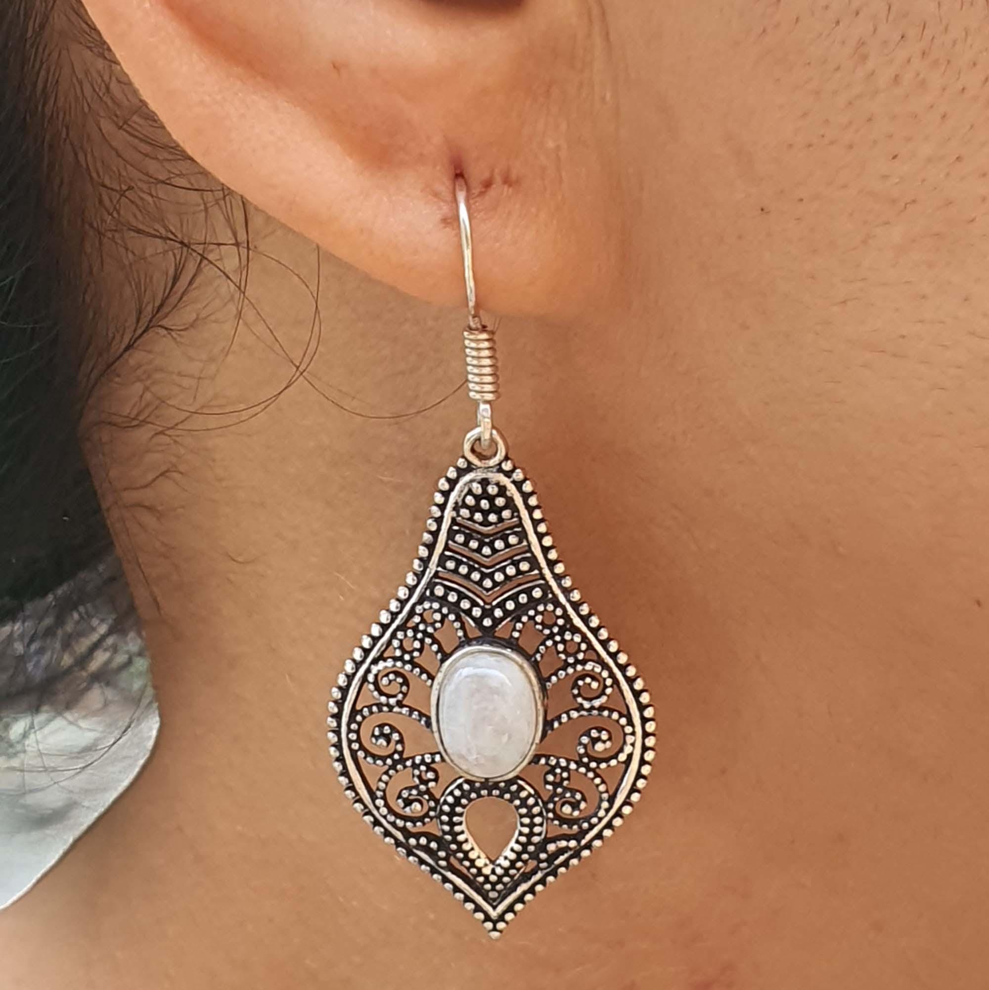 Ornate silver earring with a white stone worn by a person