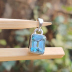 Blue gemstone pendant on a wooden stick with a blurred natural background
