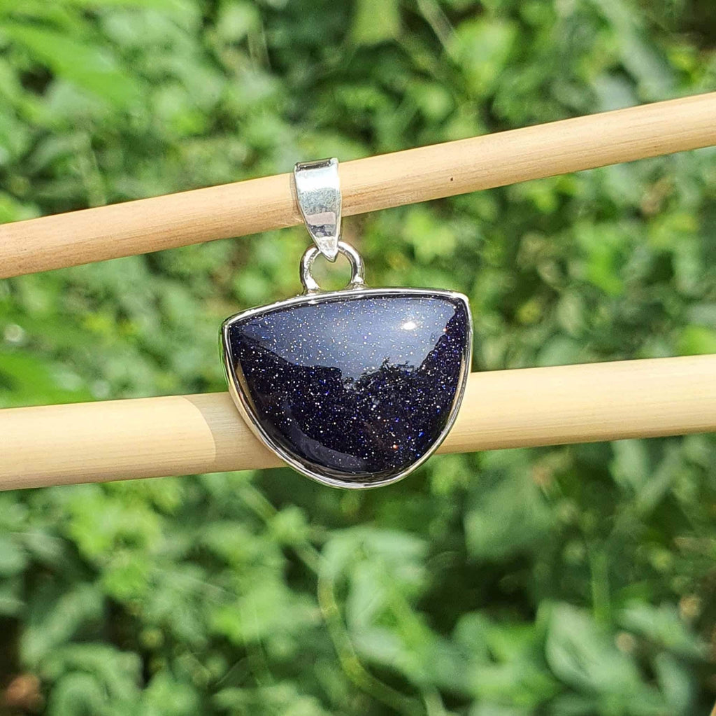 Blue stone pendant on a silver chain held by wooden sticks against a green leafy background