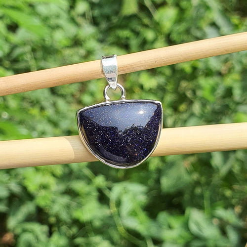 Blue stone pendant on a silver chain held by wooden sticks against a green leafy background