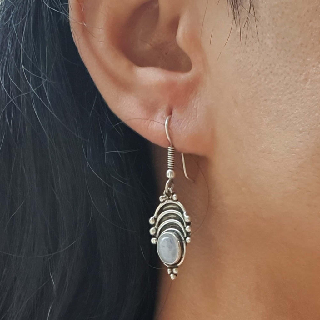 Close-up of an ear wearing a silver earring with a dark background