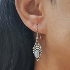Close-up of an ear wearing a silver earring with a dark background