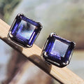 Pair of square-cut purple gemstone earrings on a wooden surface with a blurred natural background