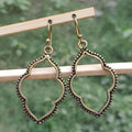 Pair of gold earrings hanging on a wooden stick with a blurred green background