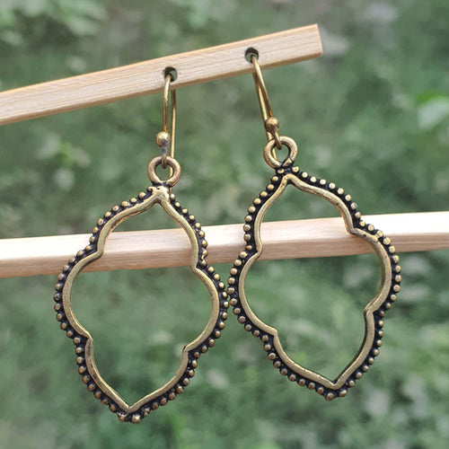 Pair of gold earrings hanging on a wooden stick with a blurred green background