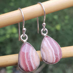 Pink marbled teardrop earrings on a wooden stick with a blurred green background