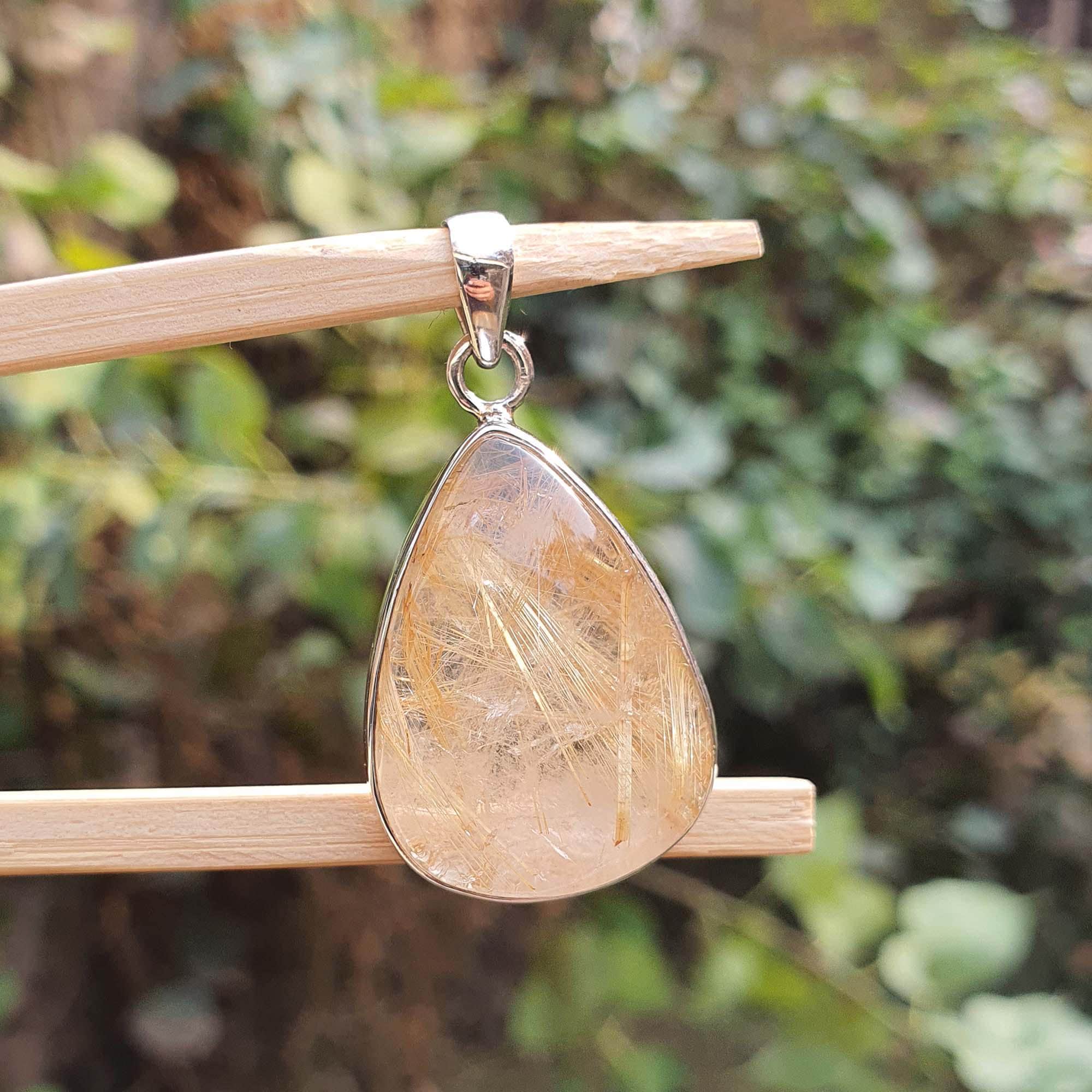Teardrop-shaped pendant with a textured surface on a wooden stick against a blurred green background