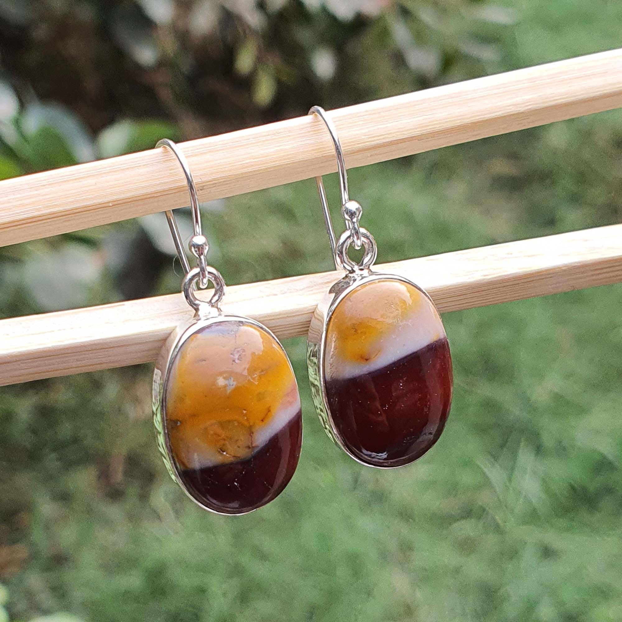 Pair of amber-colored earrings on a wooden stick with a blurred green background