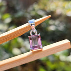 Purple gemstone pendant on a wooden stick with a blurred green background