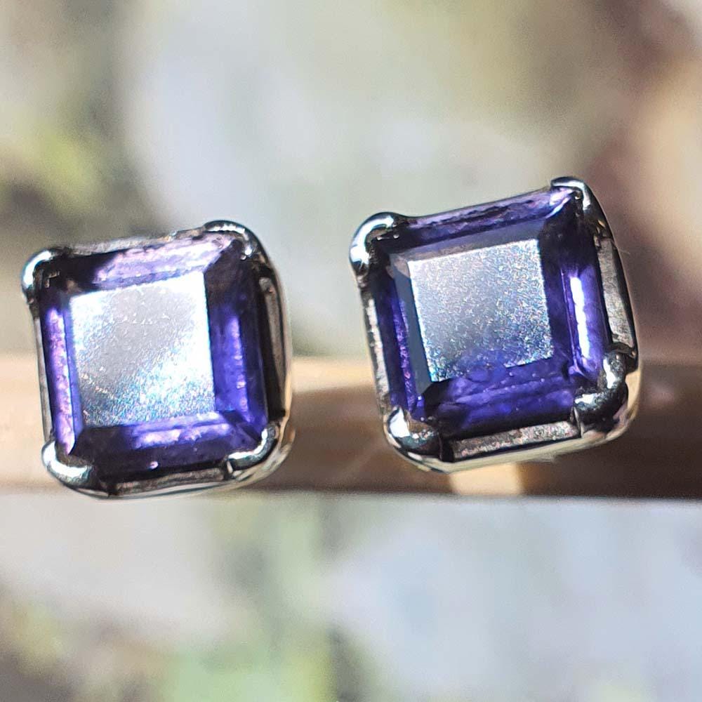 Pair of square-cut purple gemstone stud earrings on a blurred natural background