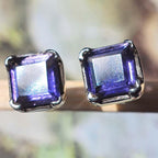 Pair of square-cut purple gemstone stud earrings on a blurred natural background