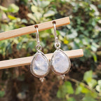 Teardrop-shaped earrings with a metallic frame on a wooden stick against a natural background.