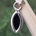 Silver pendant with a black stone on a wooden stick against a green background