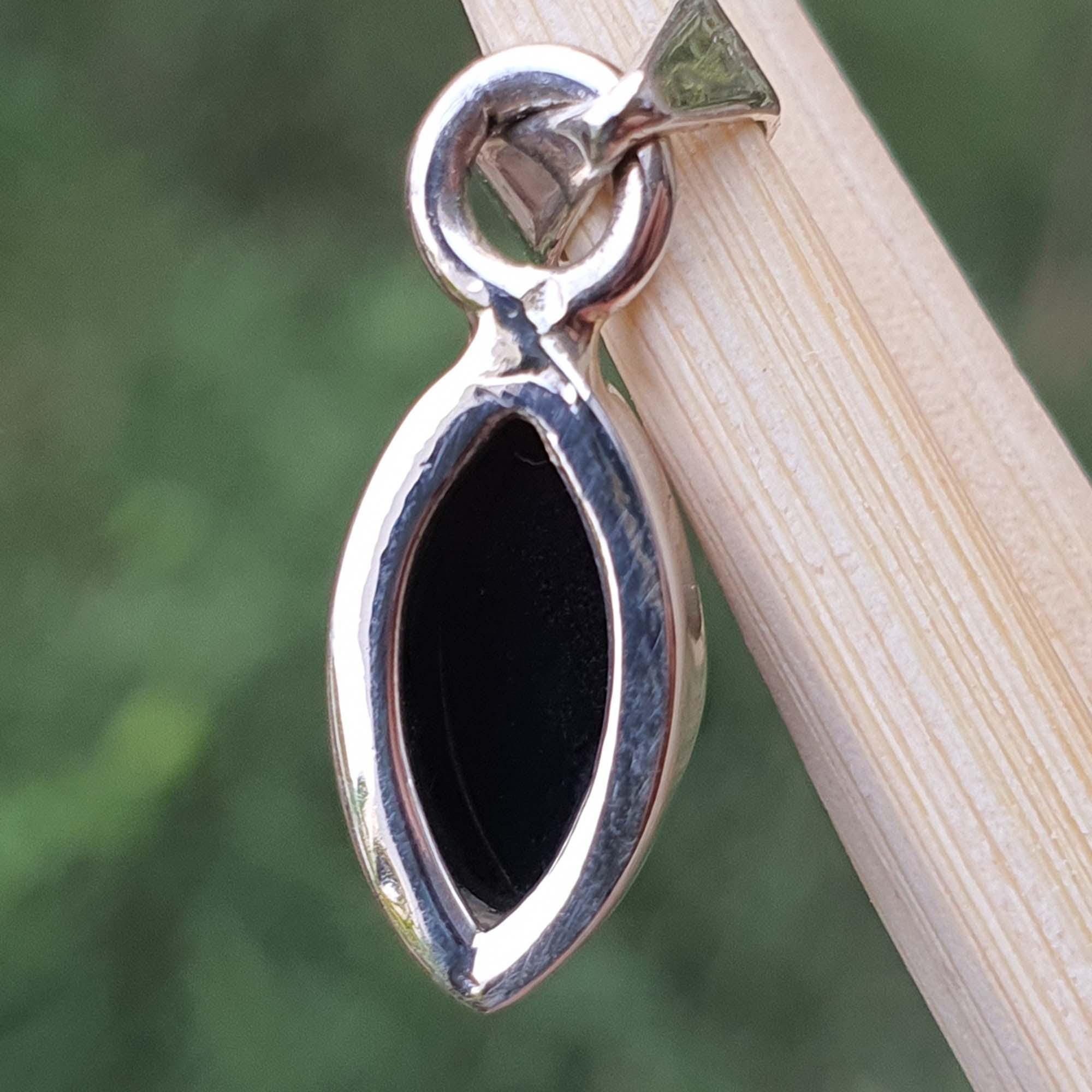 Silver pendant with a black stone on a wooden stick against a green background