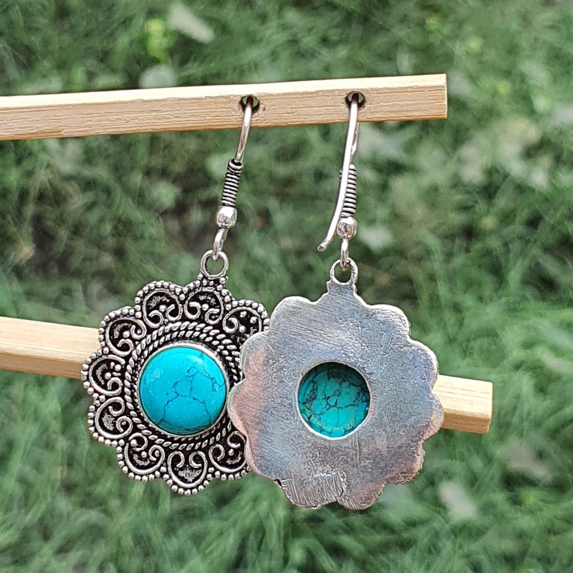 Pair of earrings with turquoise stones on a wooden stick against a green background