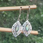 Silver earrings with green gemstones on a wooden stick against a blurred green background