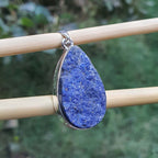 Blue teardrop pendant on a stick with a blurred green background