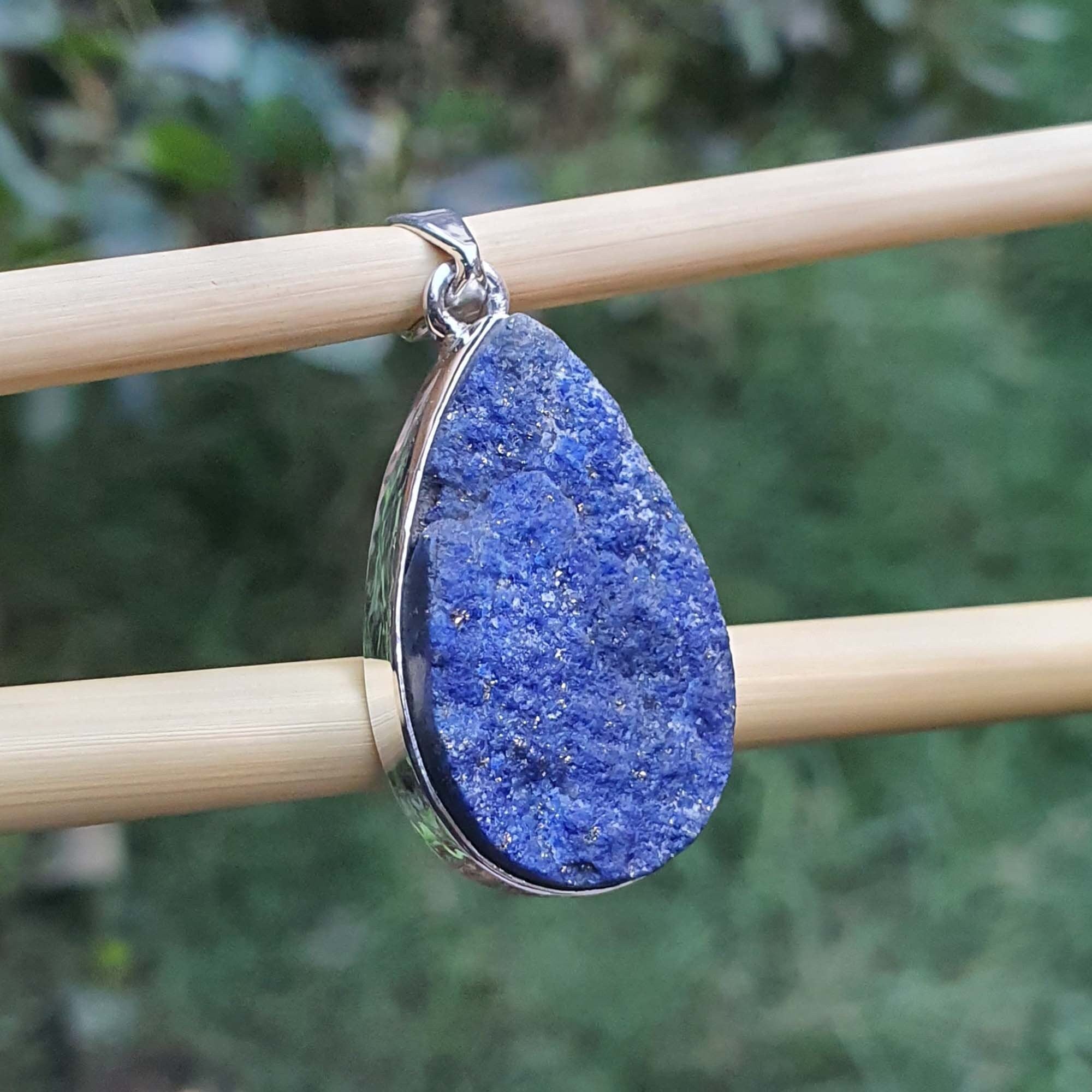 Blue teardrop pendant on a stick with a blurred green background