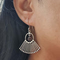 Silver earrings with a fan-like design worn by a person with dark hair.