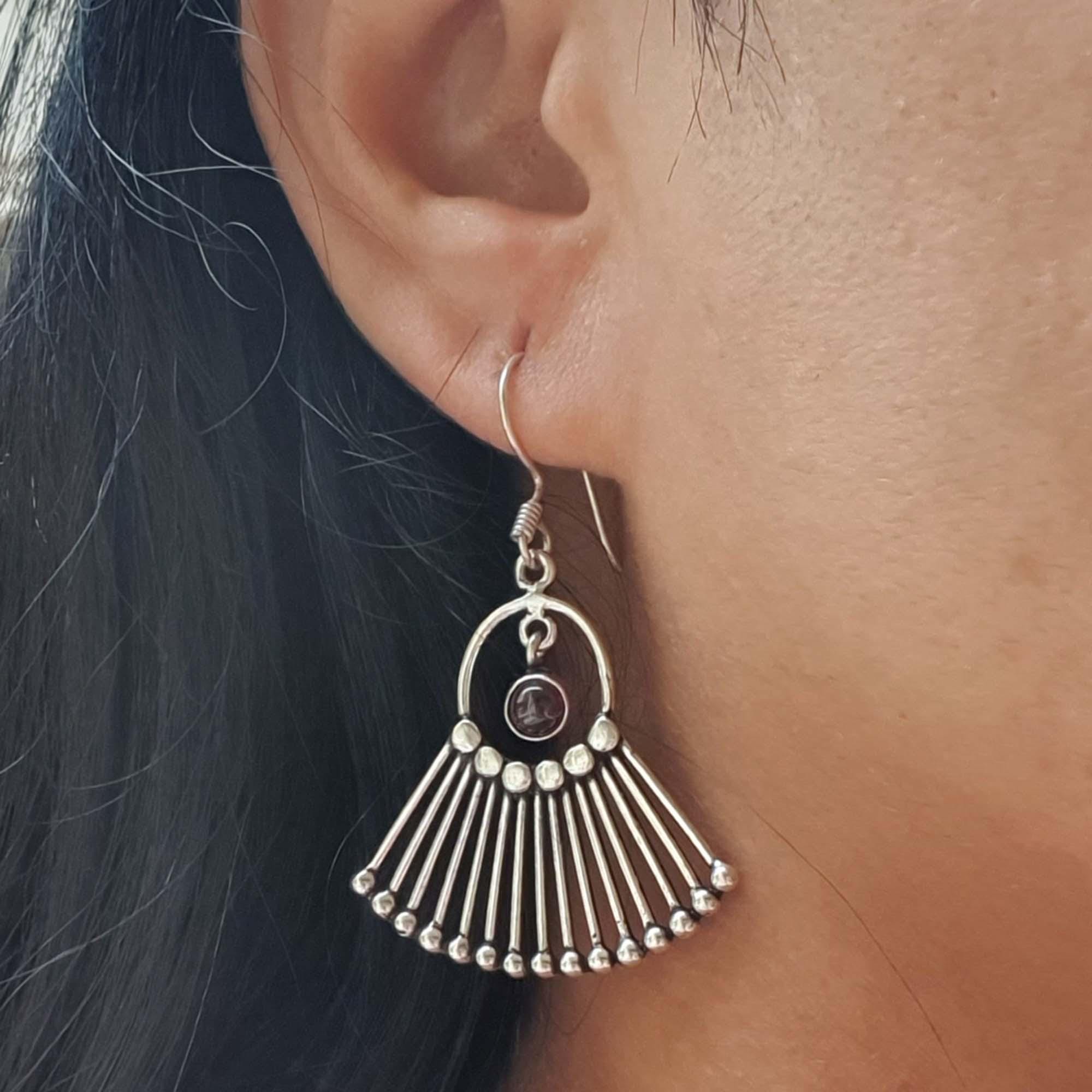 Silver earrings with a fan-like design worn by a person with dark hair.