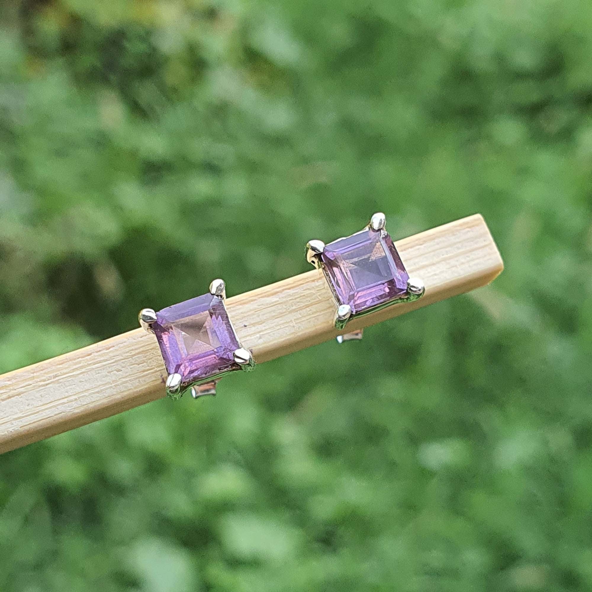 Pair of purple square stud earrings on a wooden stick with a green blurred background