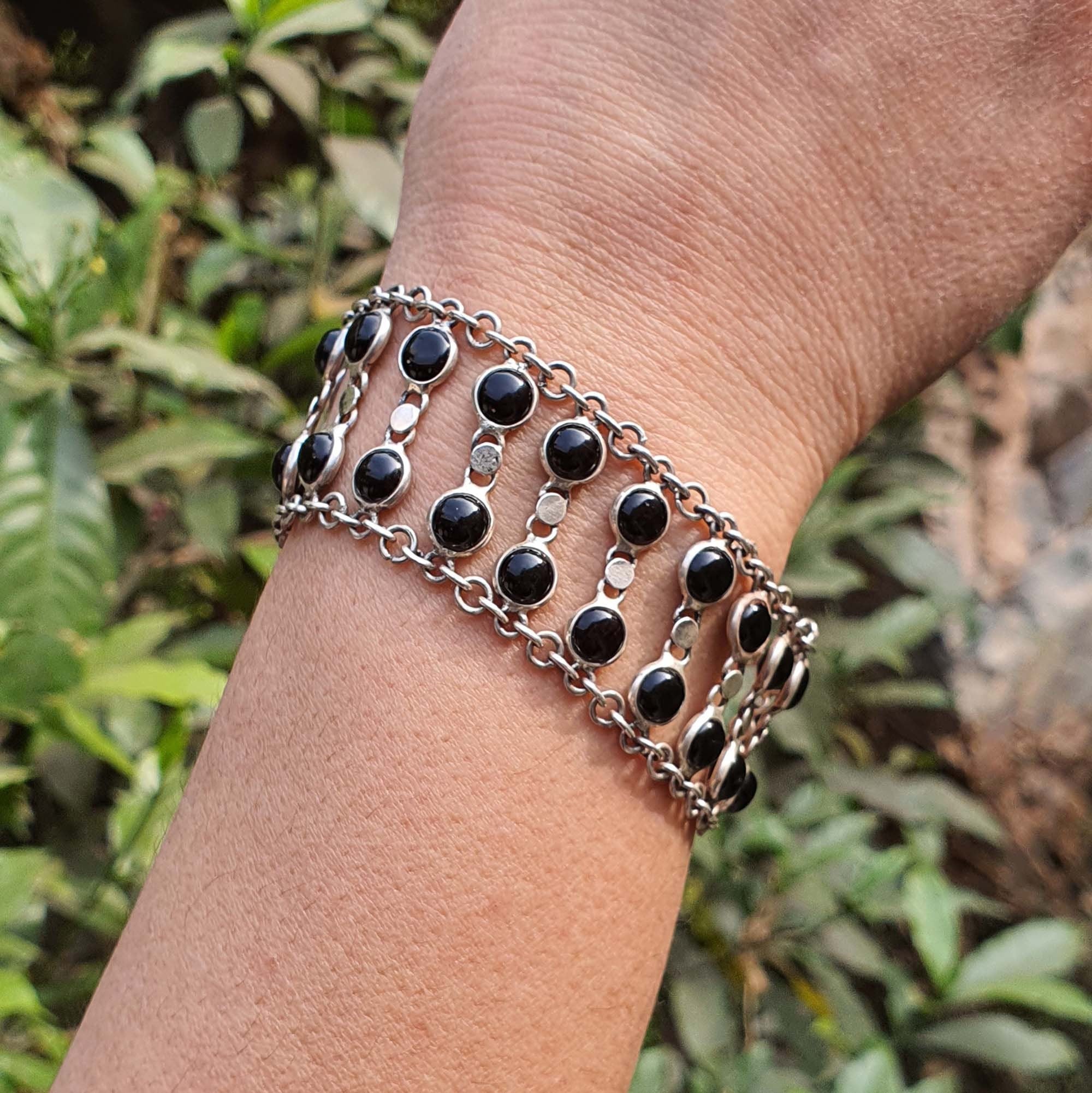 Bracelet with black beads and silver chain on a wrist against a natural background