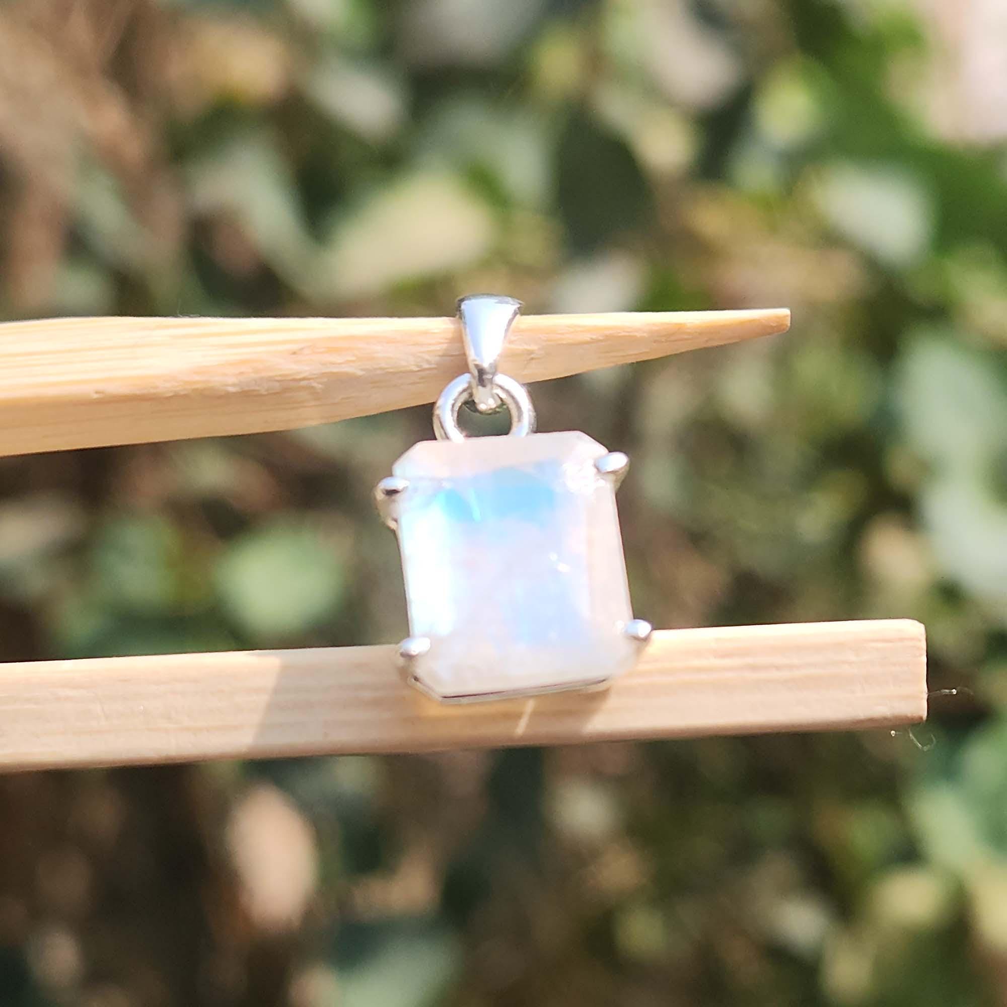 Silver pendant with a rectangular gemstone held on a stick against a blurred green background