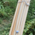 Silver necklace with a heart pendant on a wooden stick against a natural background