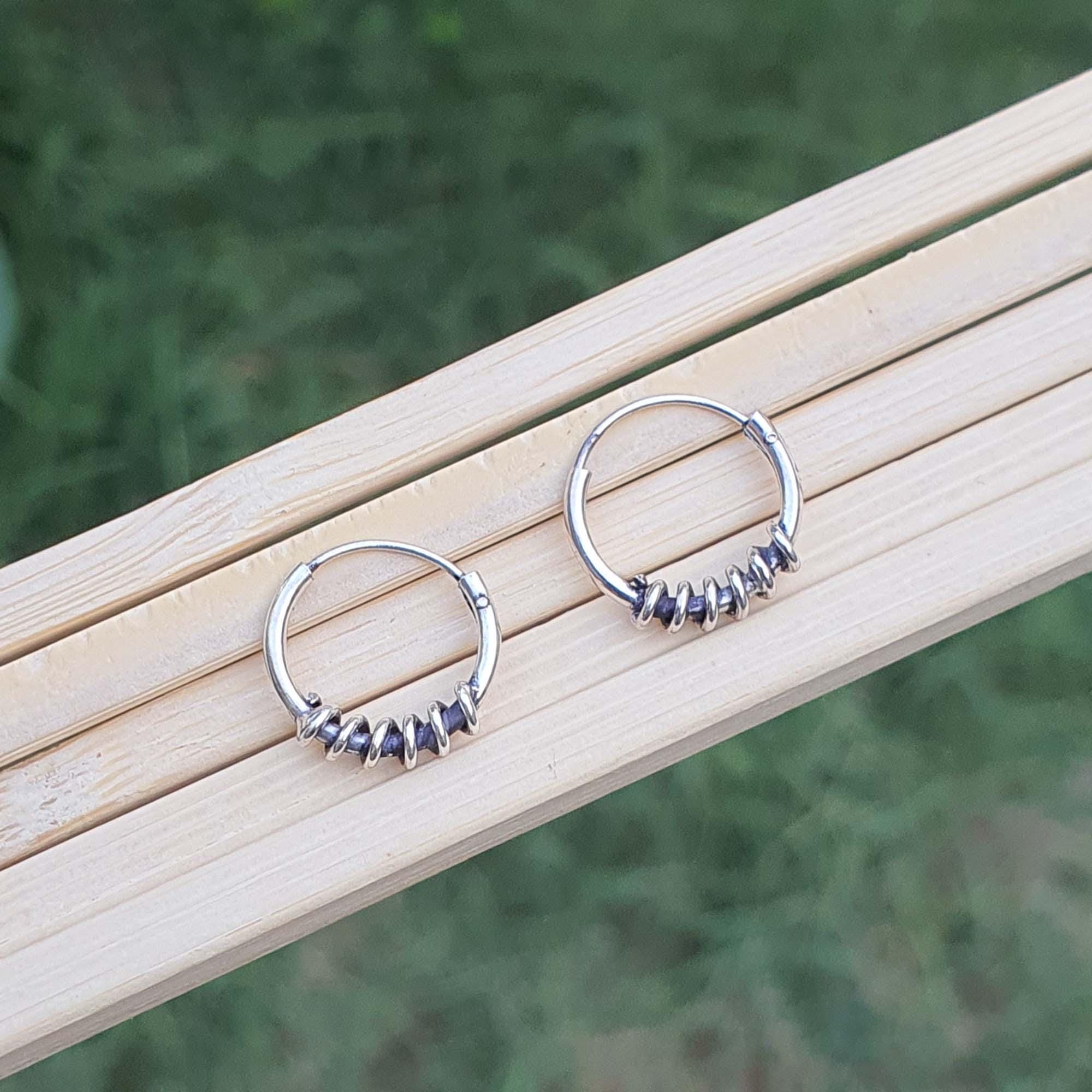 Silver hoop earrings with embedded stones on a wooden surface