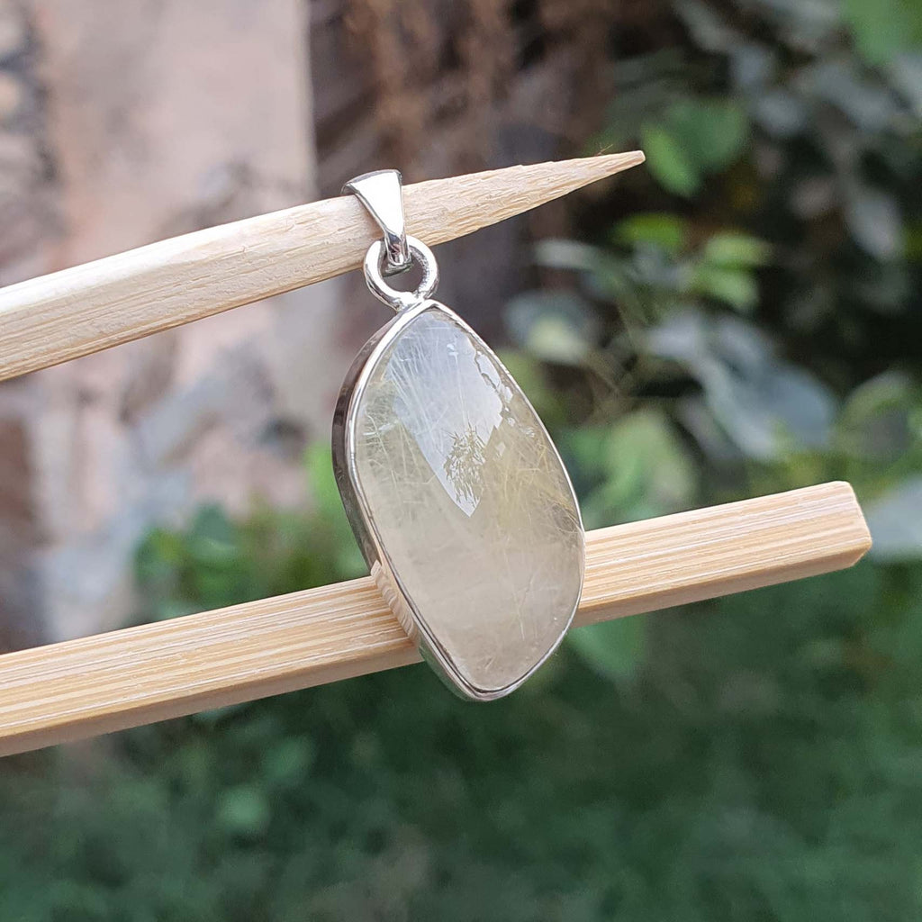 Teardrop-shaped pendant on a wooden stick with a blurred green background