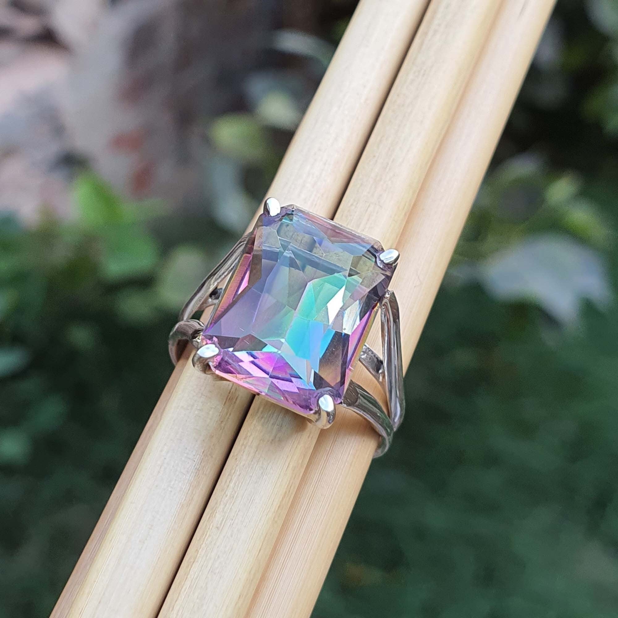 Ring with a colorful gemstone held between two wooden sticks against a blurred natural background