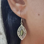 Close-up of an ear wearing a silver earring with a green gemstone.
