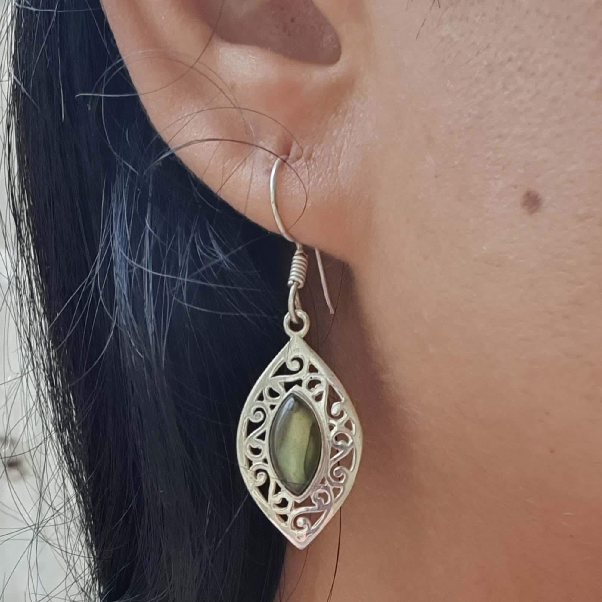 Close-up of an ear wearing a silver earring with a green gemstone.