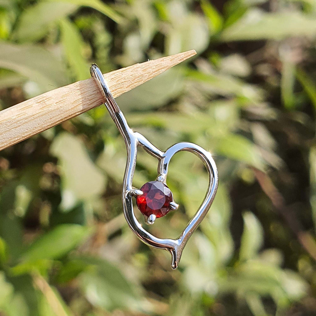 Silver heart-shaped earring with a red gemstone on a stick against a blurred green background