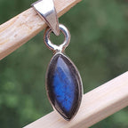 Silver pendant with a blue stone on a wooden stick against a blurred green background