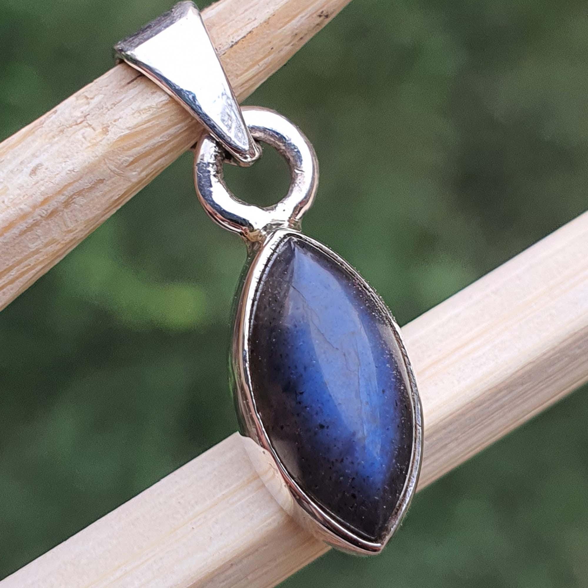 Silver pendant with a blue stone on a wooden stick against a blurred green background
