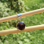 Jewelry pendant with a dark stone on a wooden stick against a green grass background