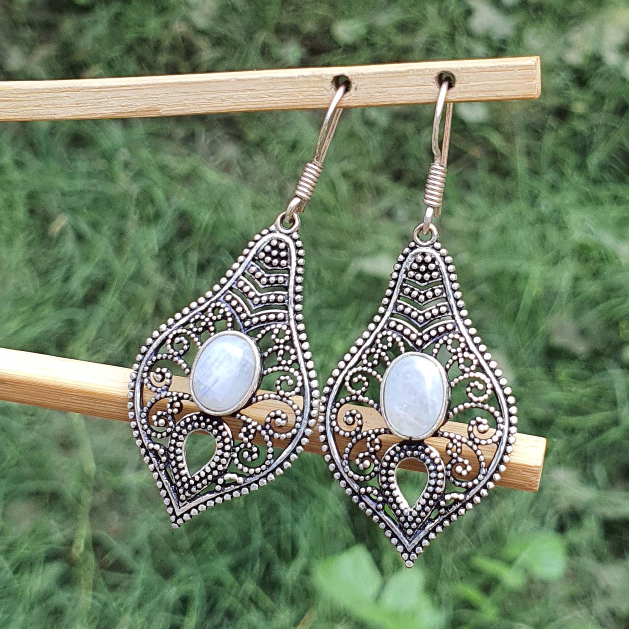 Ornate earrings with white stones on a wooden stick against a green grass background