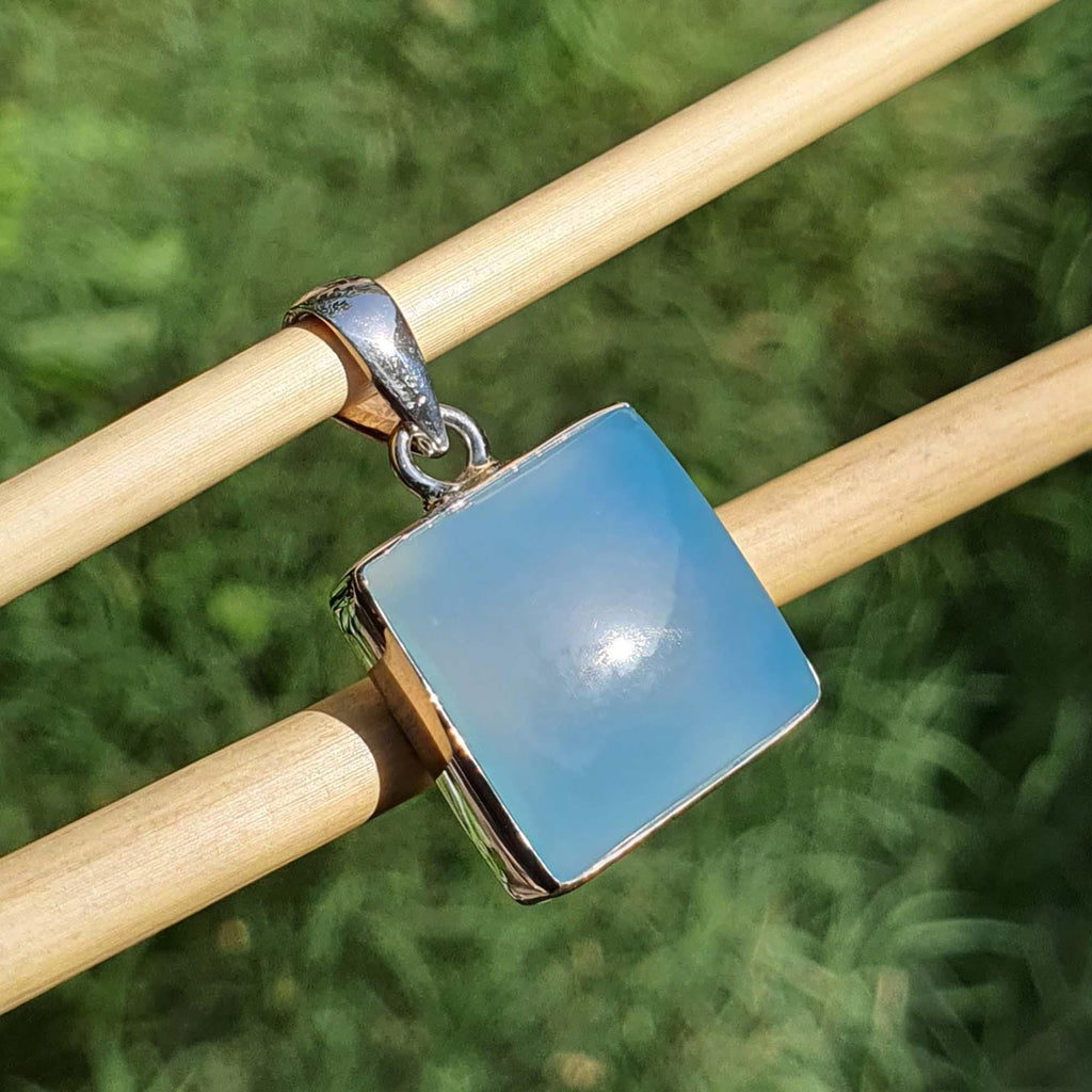 Blue square pendant on a wooden stick with a blurred green background