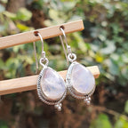 Silver earrings with teardrop-shaped gemstones on a wooden stick against a blurred green background