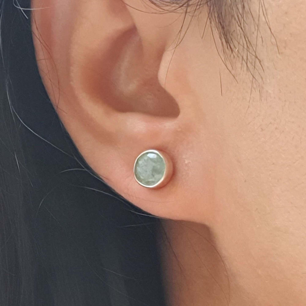 Close-up of an ear wearing a round stud earring with a green gemstone.