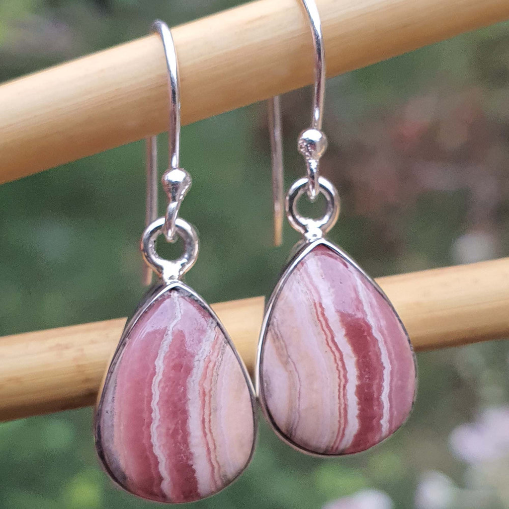 Teardrop-shaped pink and white stone earrings with silver hooks on a wooden stick.