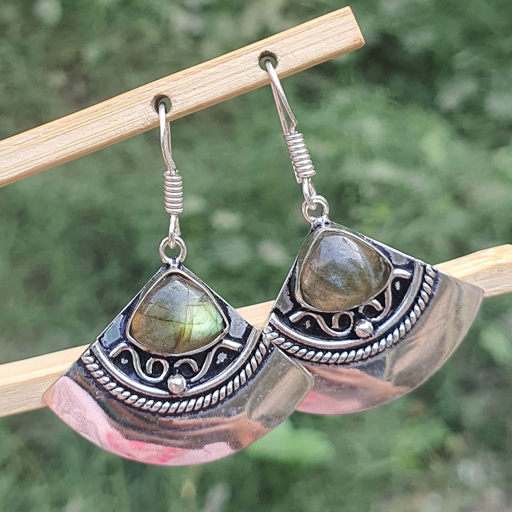 Silver earrings with green gemstones on a wooden stick against a blurred natural background