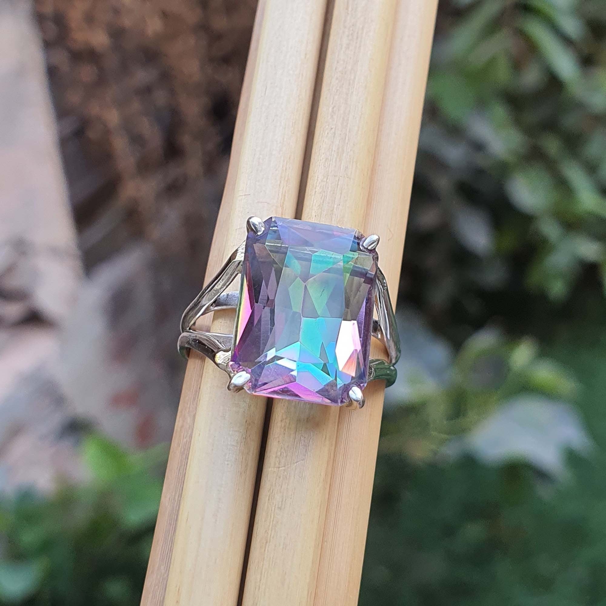 Ring with a colorful gemstone held on wooden sticks against a natural background