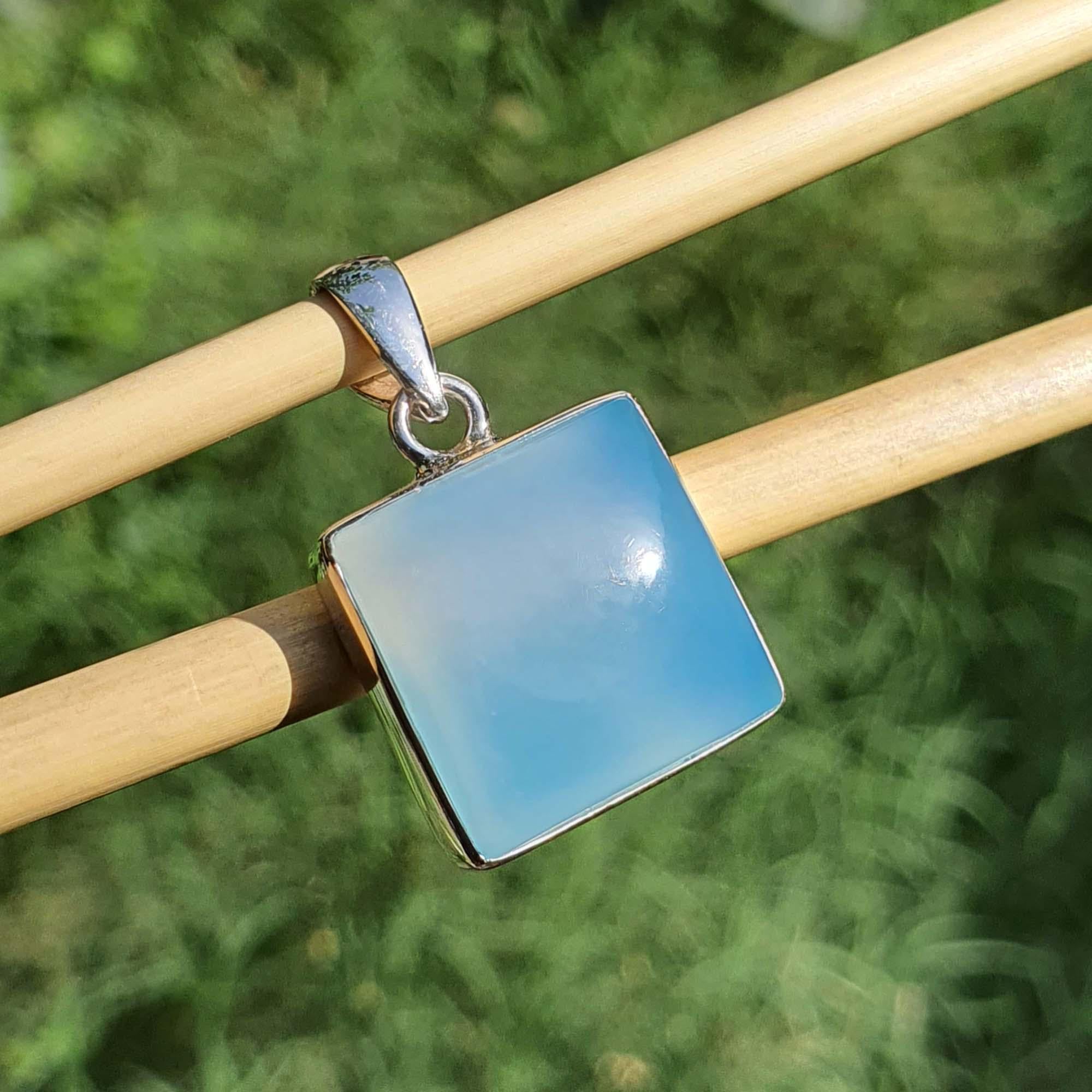 Blue square pendant on a silver chain against a blurred green background