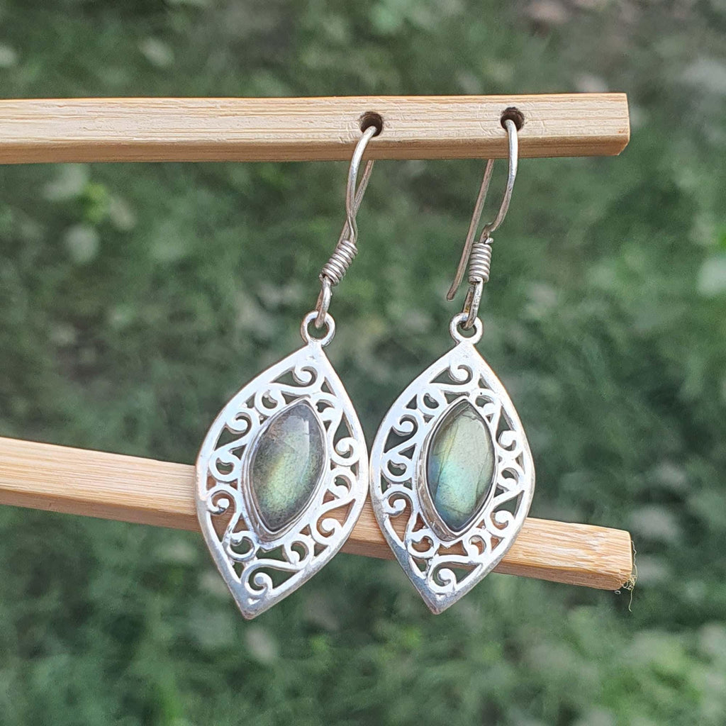 Silver earrings with green gemstones on a wooden stick against a blurred natural background