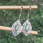 Silver earrings with green gemstones on a wooden stick against a blurred natural background