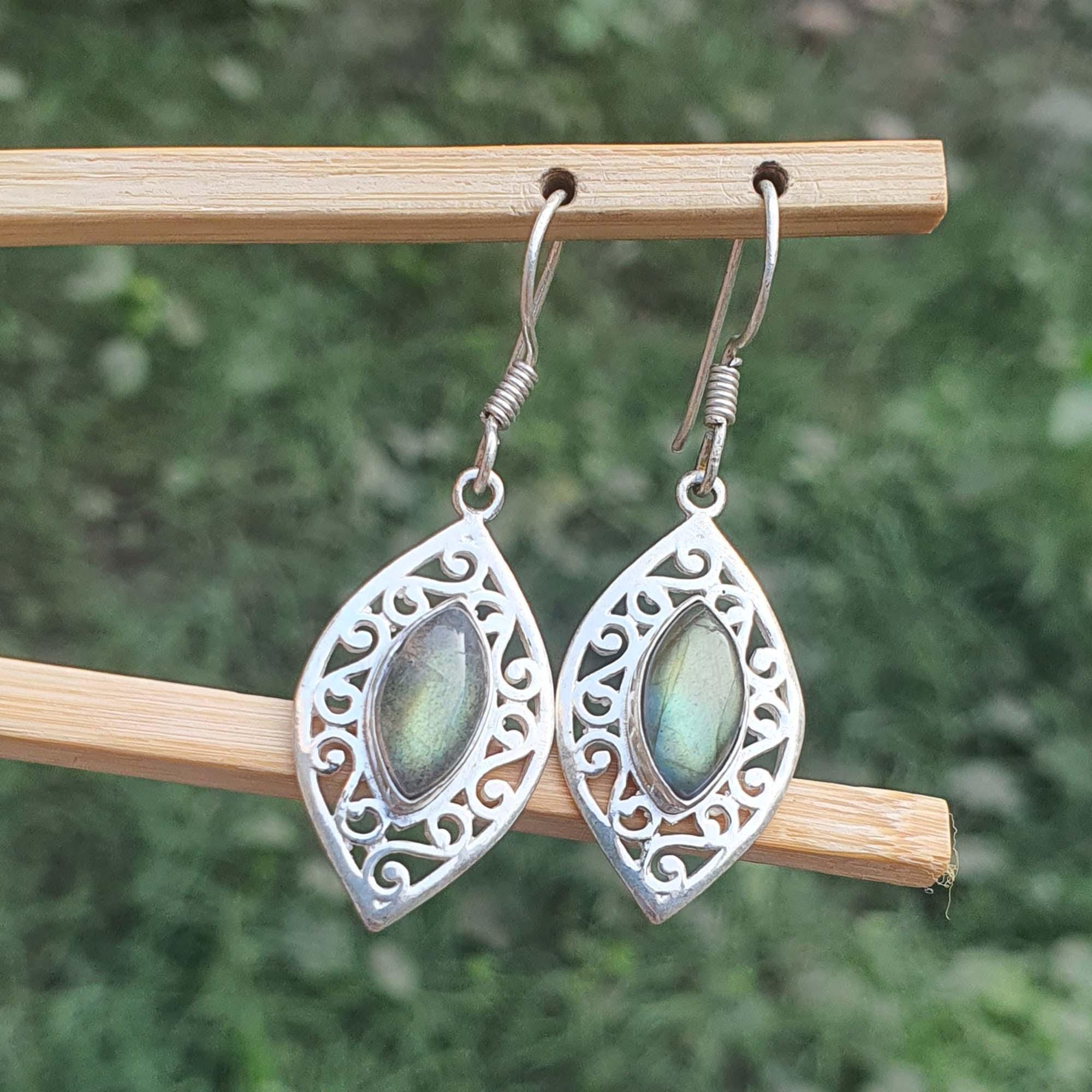 Silver earrings with green gemstones on a wooden stick against a blurred natural background